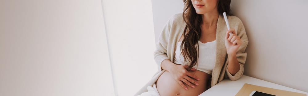 Attractive young woman holding hand on stomach and sitting in light room